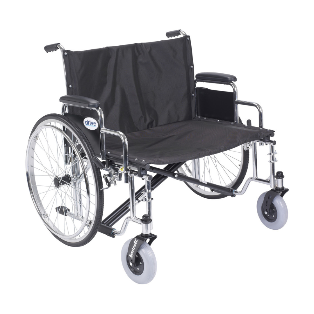 The Drive Bariatric Sentra EC Heavy-Duty Extra-Wide Wheelchair is a wide black wheelchair with large rear wheels, hand rims, padded armrests, and footrests. It is empty and shown against a white background.